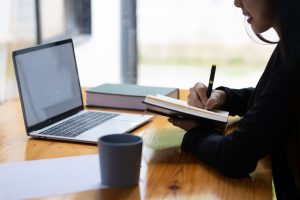 Giovane donna che prende appunti guardando lo schermo di un laptop